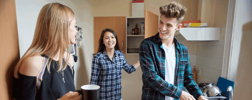 Three young people in an apartment kitchen, chatting and washing the dishes