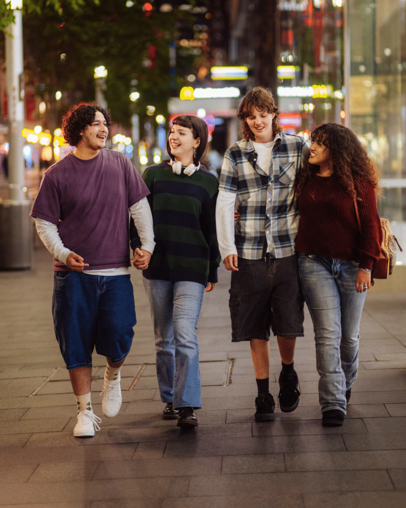 Four happy teens walk through the city at night.